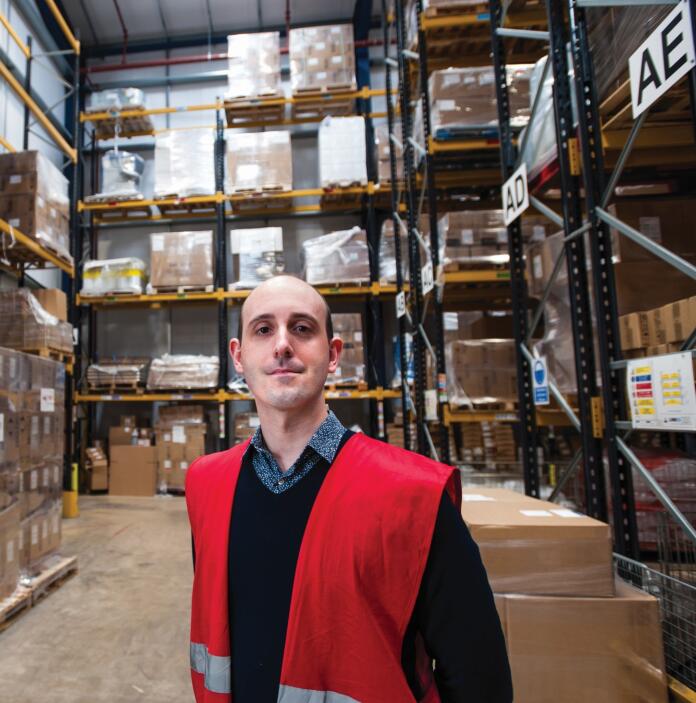 A man (Simon Owen, Head of Exports at CellPath) wearing a red safety vest standing in a warehouse