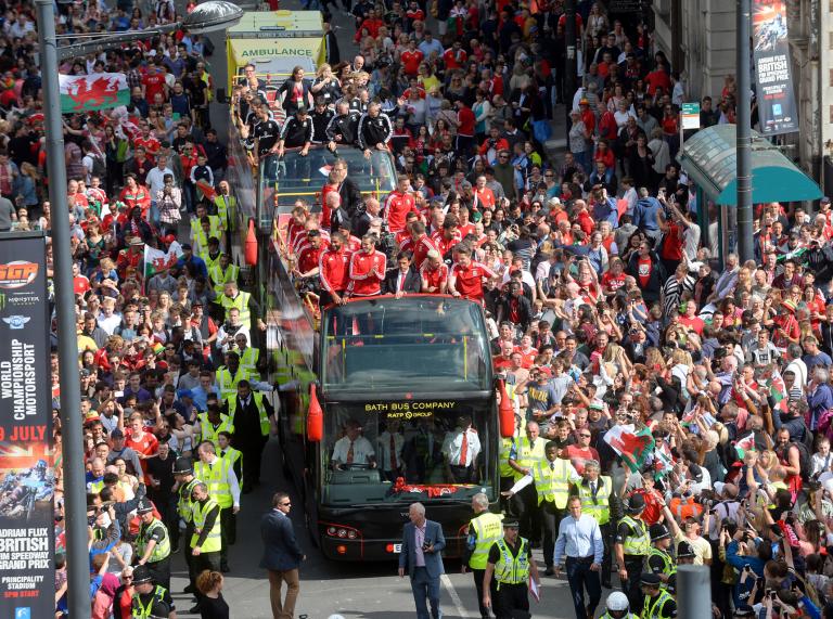 players stood on open top bus and crowds of fans in street.