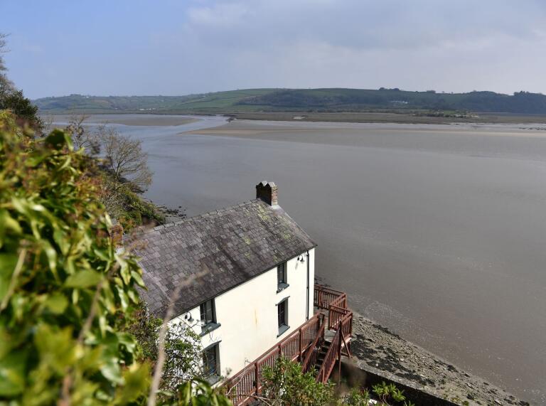 An old white house on the banks of a cliff overlooking an estuary