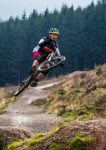 A mountain biker takes a large jump in a forested mountain bike park