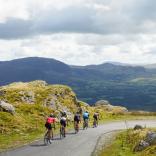 Five people on road bikes cycling down a scenic road against the backdrop of mountains