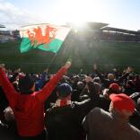 サッカーの試合を応援する観客。スタジアムの座席ではウェールズの国旗がはためいています。
