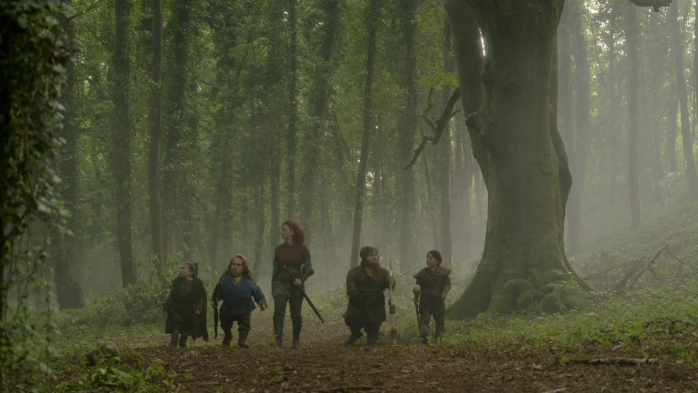 (L-R): Mims (Annabelle Davis), Willow Ufgood (Warwick Davis), Jade (Erin Kellyman), Karthy (Simeon Dyer) and Nelwyn Villager (Arti Shah) walking through a misty woodland in Lucasfilm's Willow.