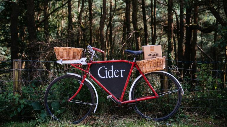Un vélo de livraison rouge affichant le mot « cidre »et du cidre Hallets dans les paniers en osier.
