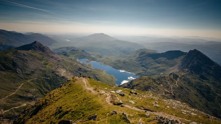 Panoramic view from Yr Wyddfa in Eryri (Snowdonia) National Park, North Wales, overlooking rugged mountain peaks, winding paths and lakes. 