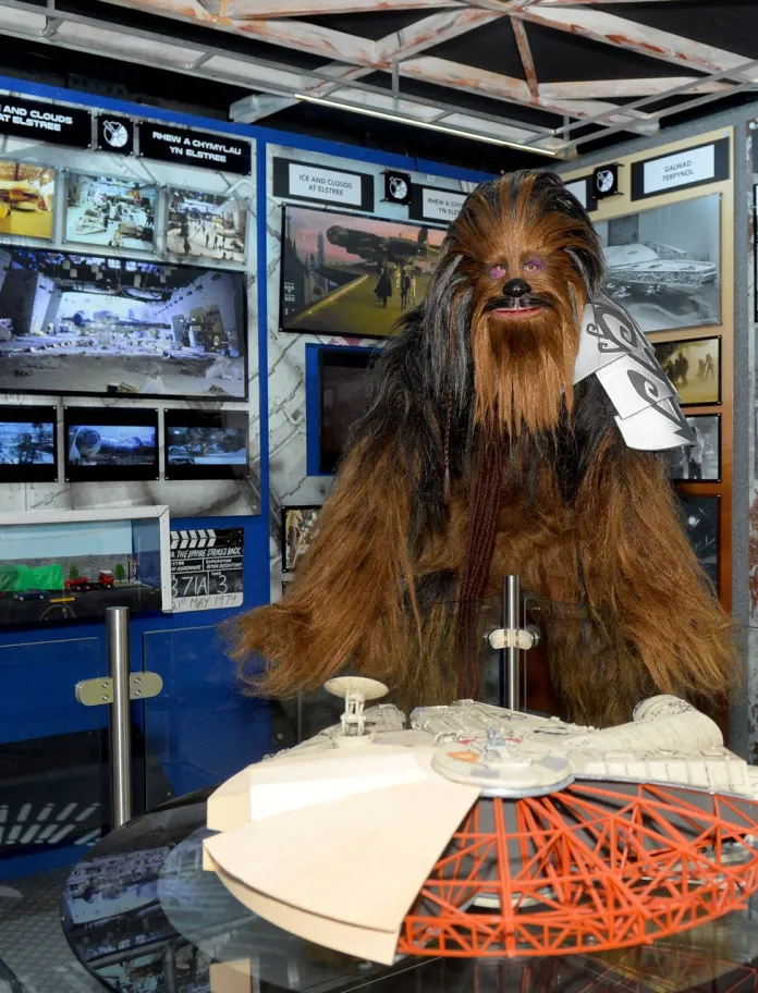 Chewbacca standing behind a model of the Millennium Falcon in a Star Wars exhibition.