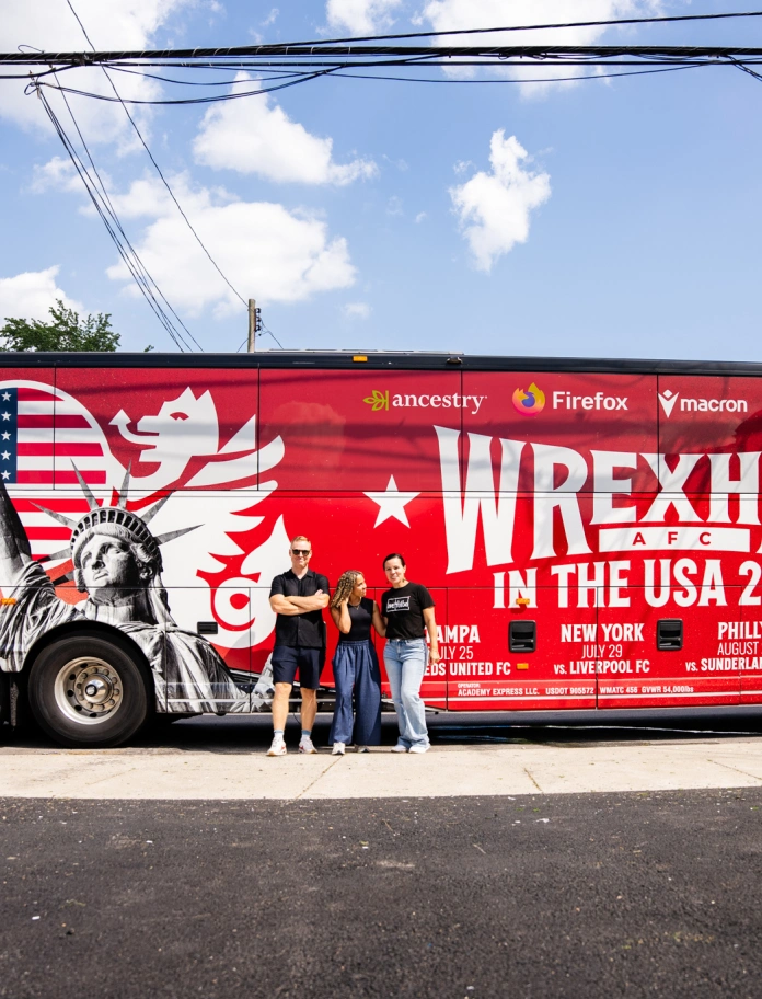 Three people standing in front of the Wrexam AFC tour bus