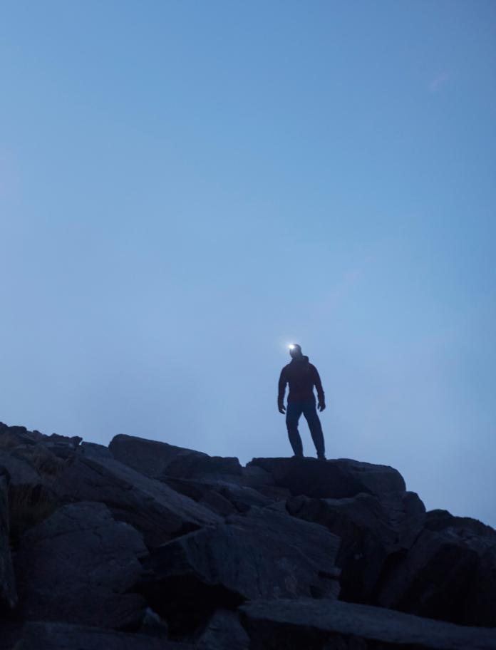A silhouette of a man standing on the edge of a mountain at dusk