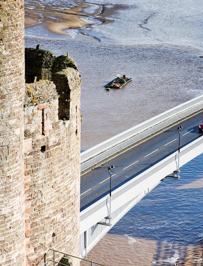 Image of a red car driving on a bridge towards Conwy Castle