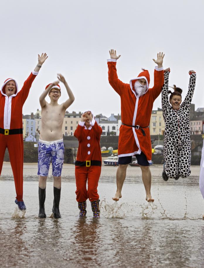 Leute in weihnachtlichen Kostümen springen aus dem Meer in die Luft.