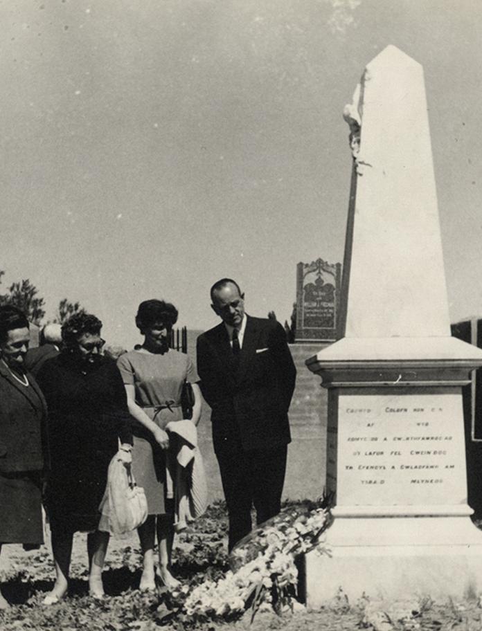 Group of 4 people standing looking at a memorial in the grounds of Moriah Chapel, Trelew. Standing extreme left is Robin Gwyndaf.
