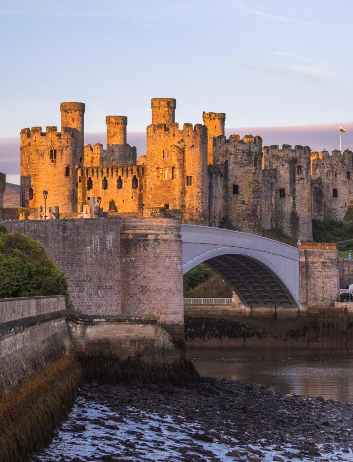 View of a historic castle which lies behind a bridge by sunset. 