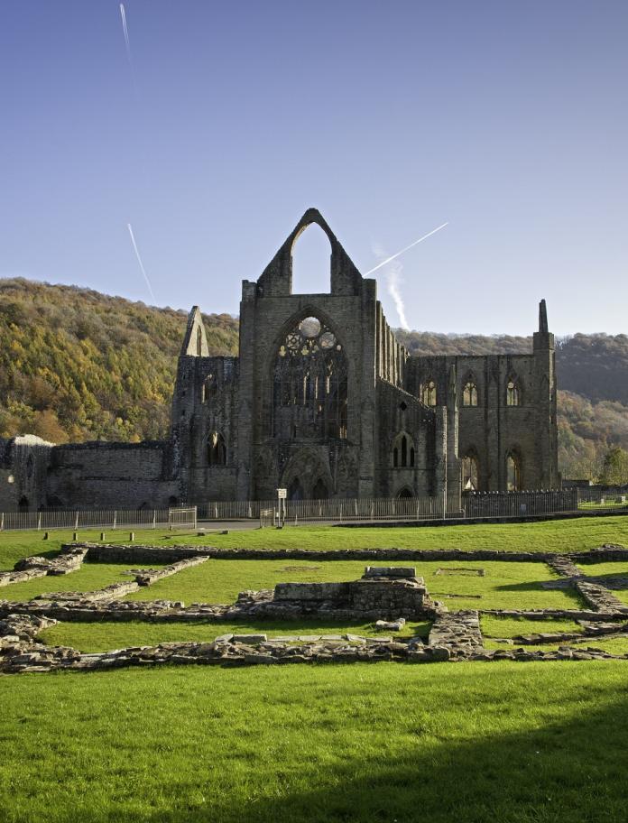 Ruins of an old abbey surrounded by green fields, hills and blue skies.