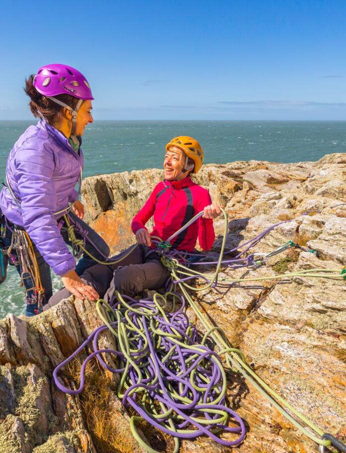 Female rock climber reaching top of sea cliff at Rhoscolyn, Holy Island, Anglesey.