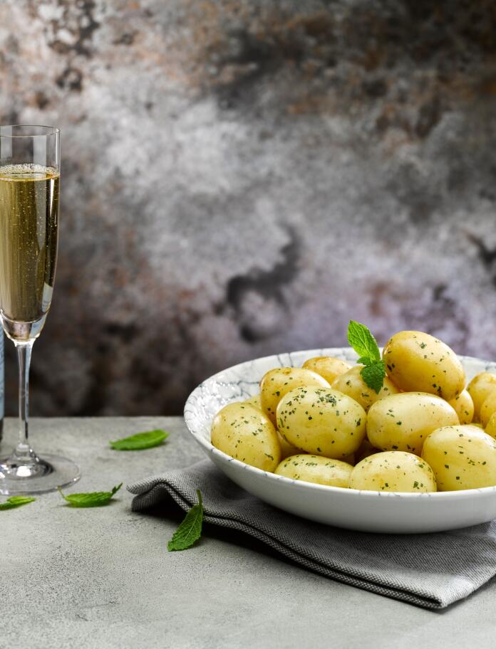 A bowl of potatoes next to a bottle and glass of champagne.