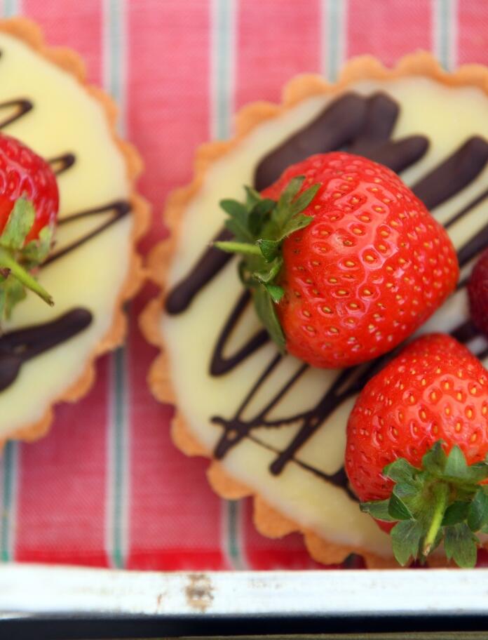 TwoTop down view of two strawberry and chocolate topped tarts on a red and white striped background.