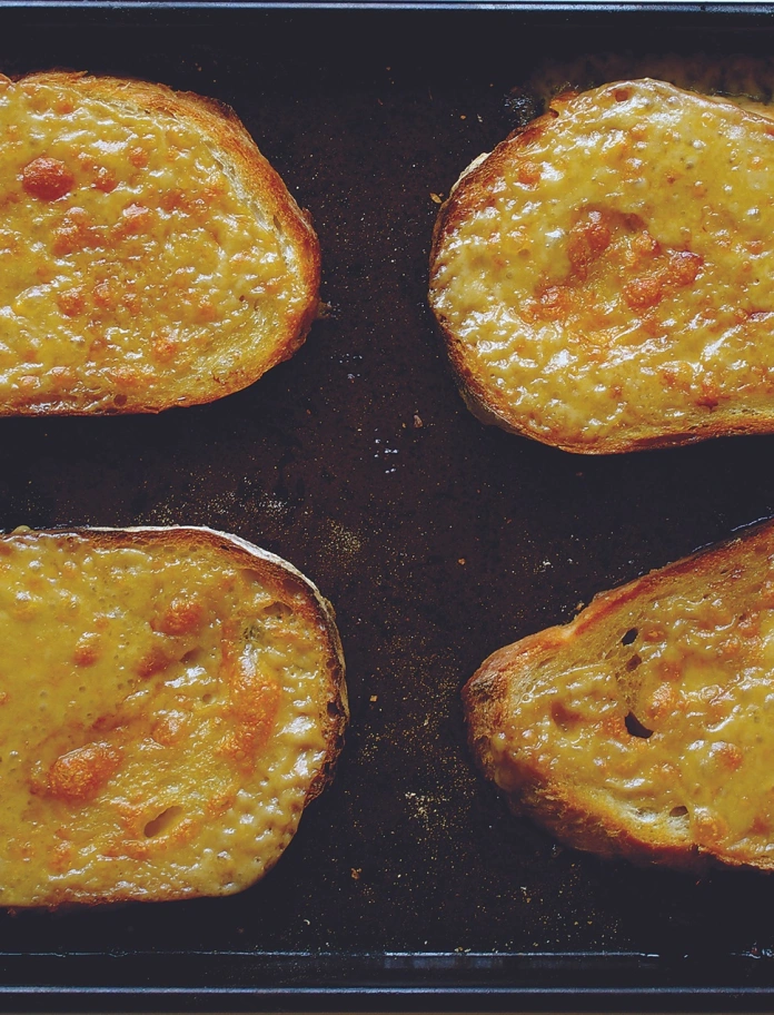 Trois tranches de Welsh rarebit sur un plateau noir.