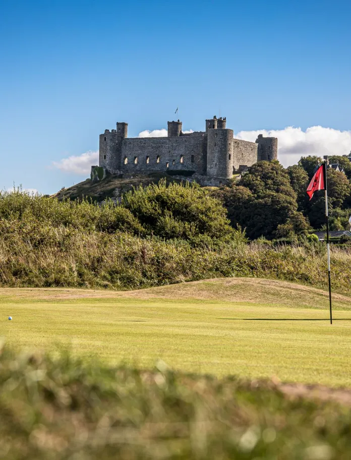 Golfers playing on a scenic course with an ancient castle and distant village nestled on a hill.