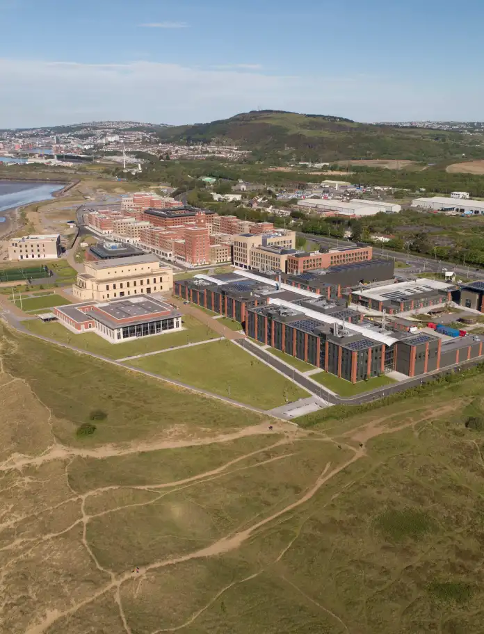 The Swansea University campus building next to grass and the sea.