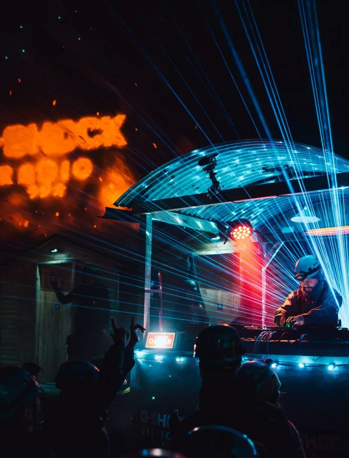 DJ Roni Size performing at an underground rave in Cwmorthin, with blue laser lights illuminating the cavern and crowd. 