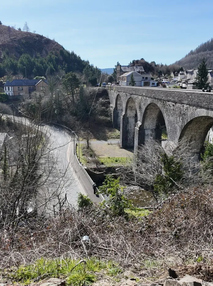 A stone bridge over a road surrounded by trees.
