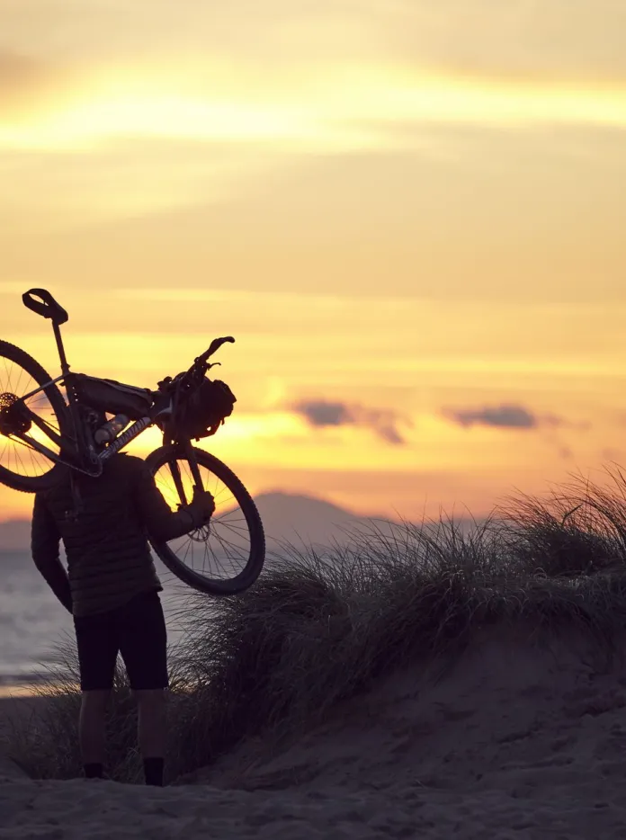 Richard Parks holding a bike on his shoulders with a sunset in the background