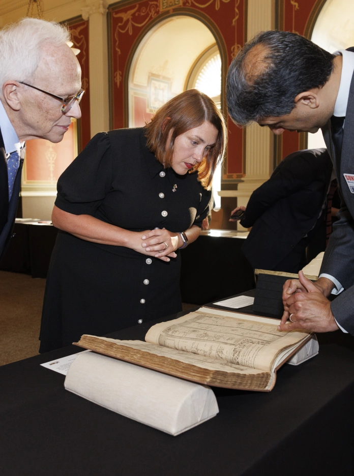 Three people examine a historic music manuscript on display at the Library of Congress. 