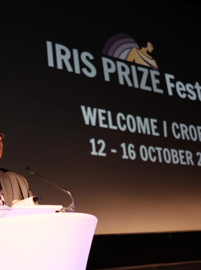 Berwyn speaking at a lectern on stage during the Iris Prize Festival in 2016.