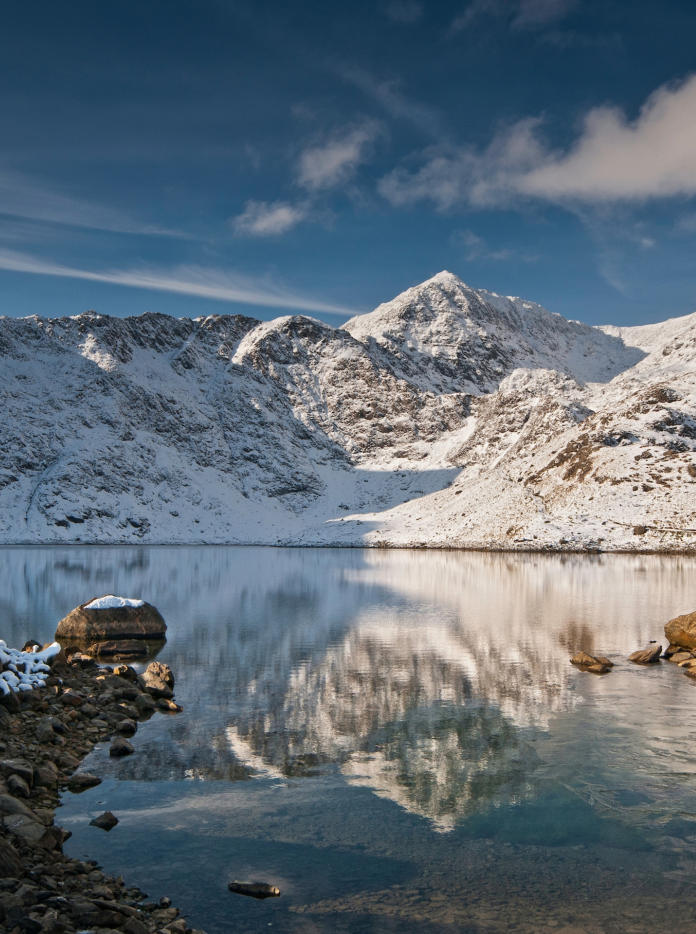 Walker looking towards snow-covered summit of Yr Wyddfa (Snowdon)from Llyn Llydaw lake, Snowdonia