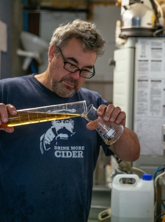 Cider maker Andy Hallett pours cider from one measuring container to another.
