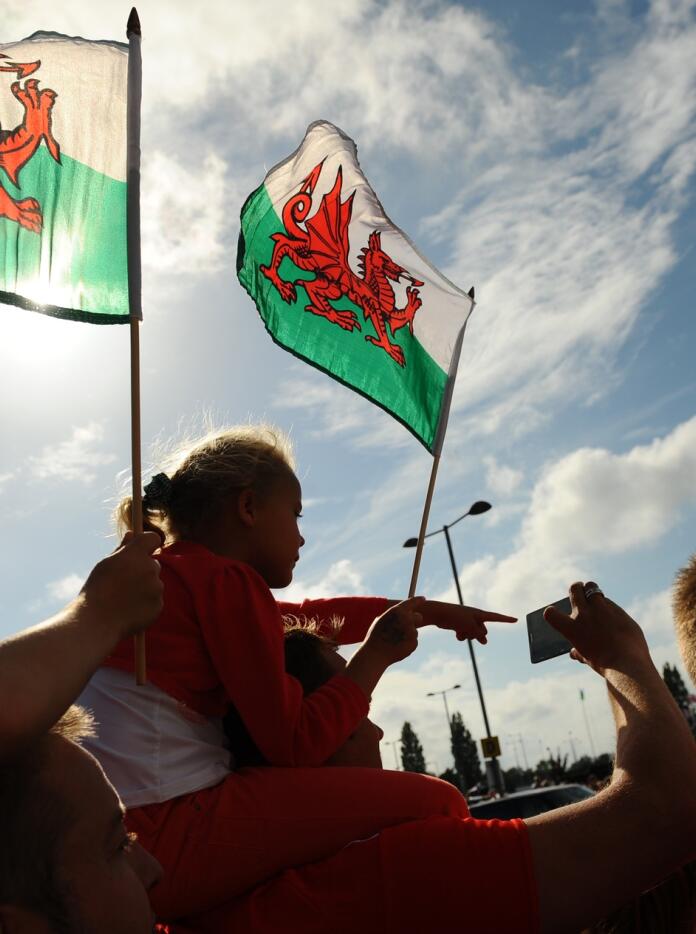 The silhouette of three people holding Wales flags.