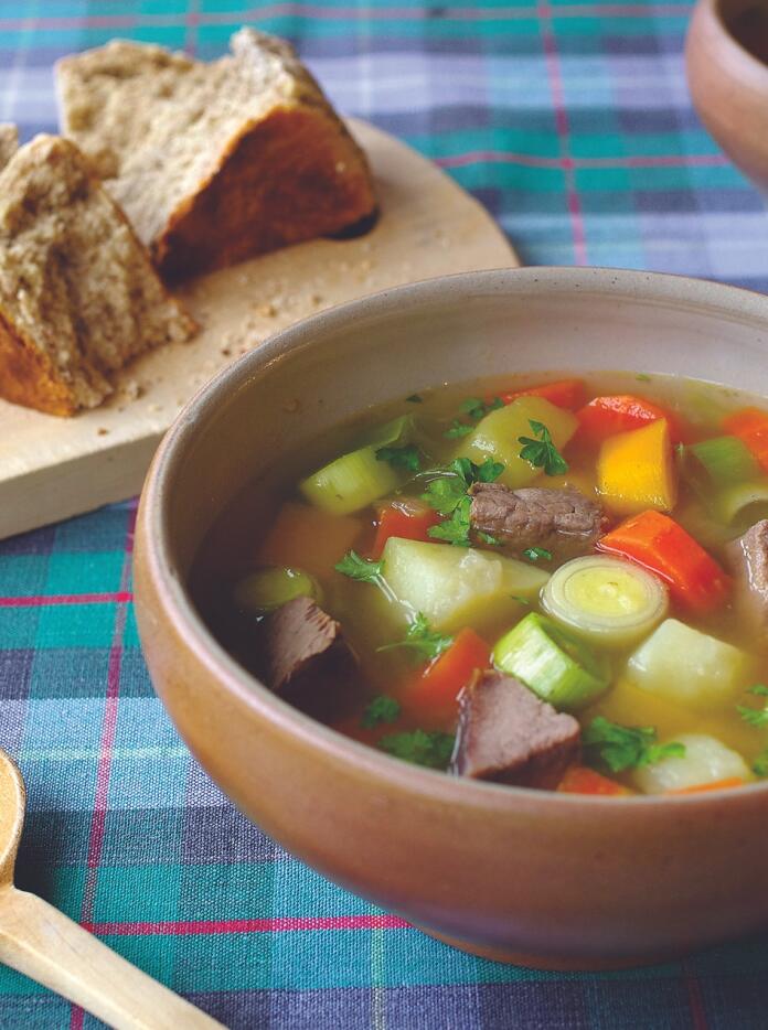 A bowl of soup with meat and vegetables, next to some crusty bread.