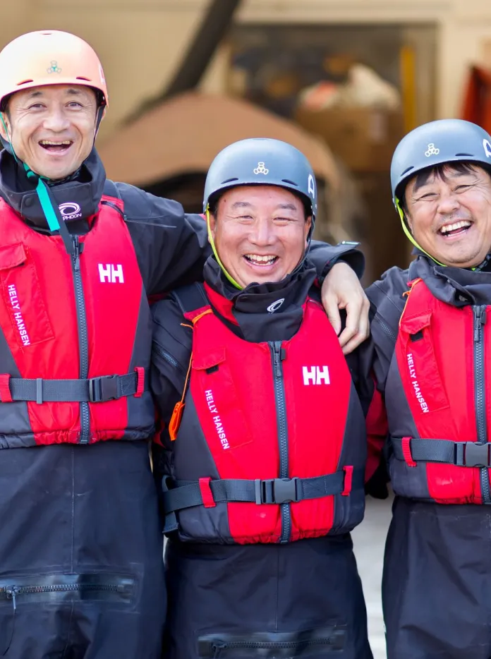 Tres bomberos japoneses estaban de pie uno junto al otro, sonriendo con ropa de rescate marítimo, en el UWC Atlantic College.