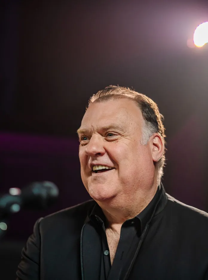 Sir Bryn Terfel standing in front of a microphone and smiling.
