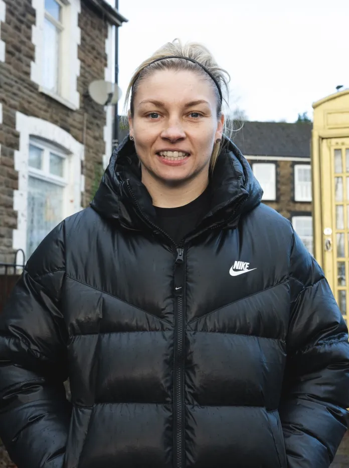 Lauren Price MBE stands beside a traditional yellow telephone box on a street in her hometown of Ystrad Mynach. 