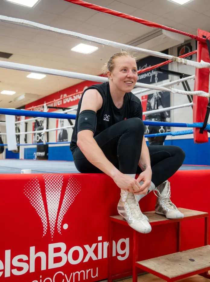 Rosie Eccles smiles as she laces up her boxing boots beside the ring before training.