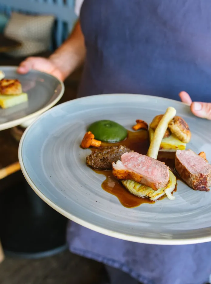 A person carrying two plates of roast Lamb