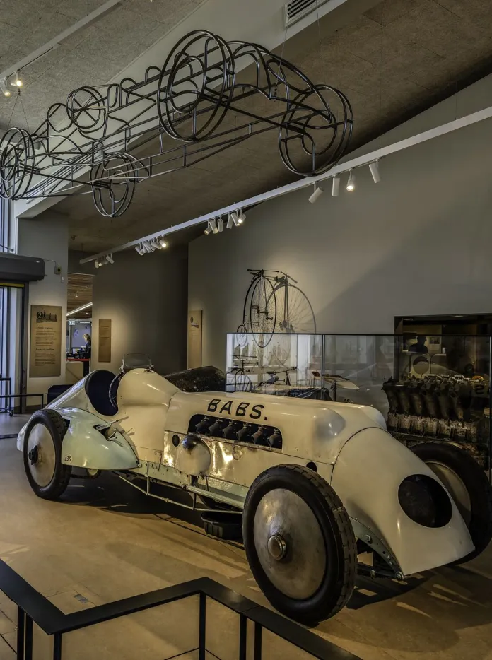 Historic white racing car Babs, driven by JG Parry-Thomas, displayed inside the Museum of Land Speed in Pendine, with a wireframe car suspended above. 