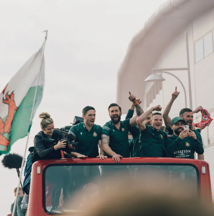 Wrexham football players on the top of a bus with the Welsh flag.