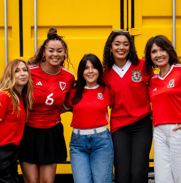 A group of people wearing Welsh football shirts smiling at the camera