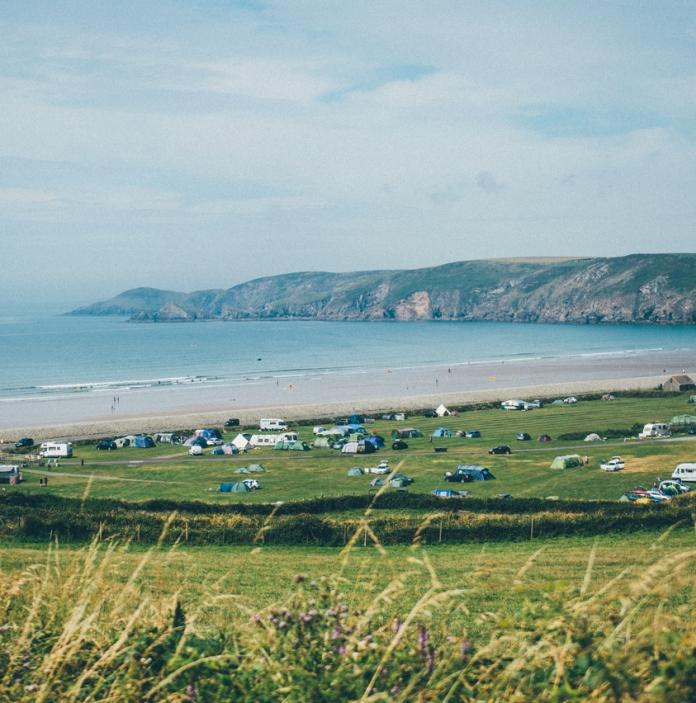 Blick von der Spitze eines Hügels auf den Strand und die Küstenlinie mit Wohnwagen und Zelten auf dem Feld