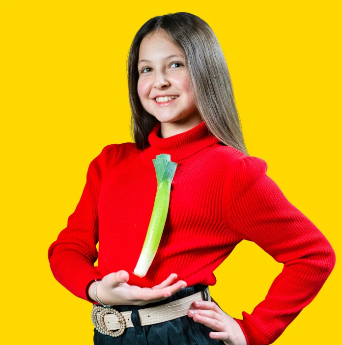 Jeune fille portant un chapeau gallois et un pull rouge sur lequel est épinglé un poireau