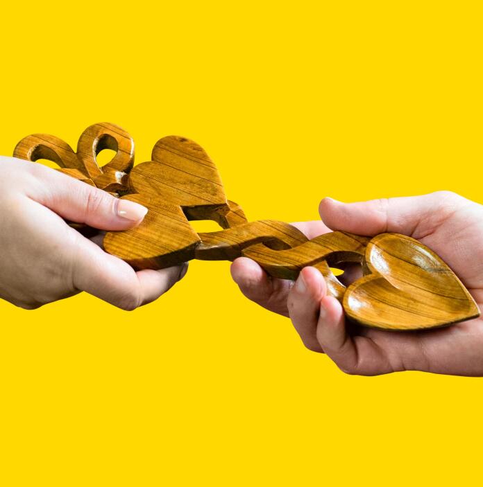 Deux mains qui se tiennent et une “love spoon” (cuillère d’amour) sur un fond jaune