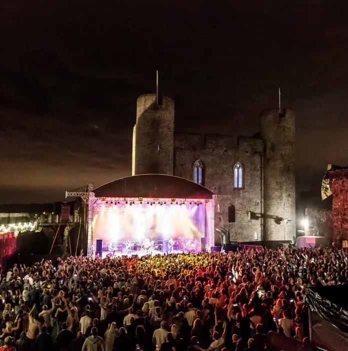 Une scène de concert dans l’enceinte d’un grand château, avec une foule de spectateurs
