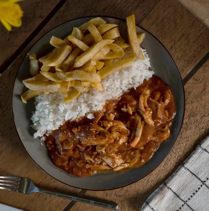 Une assiette de curry au poulet avec du riz et des frites sur une table avec une nappe à carreaux et des jonquilles dans un vase