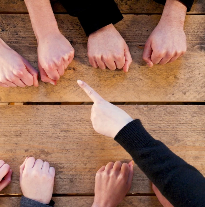 Un groupe de personnes avec les poings fermés sur la table, et une main qui pointe à l’un des poings