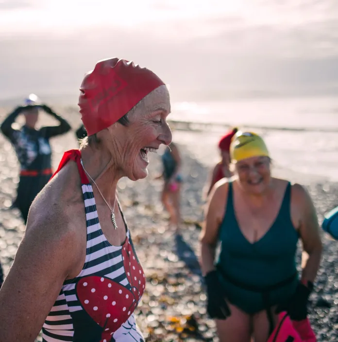 26 Membre d’un club de nage gallois fait des éclaboussures et sourit dans la mer à Ynyslas, entourée d’amis