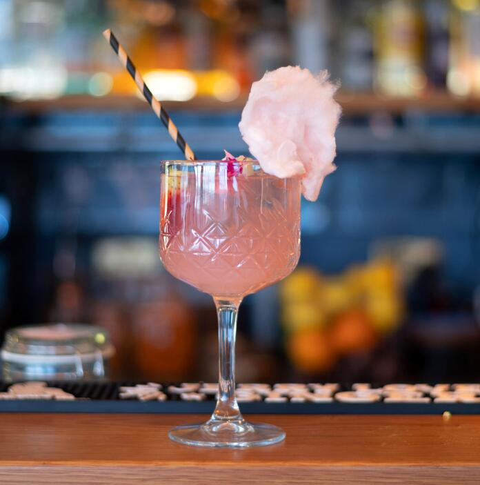 A pink cocktail in a pretty glass with striped straw and flower garnish