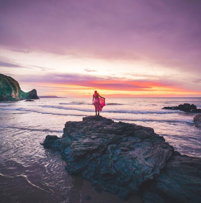 A person standing on a rock in front of an amazing purple sunset