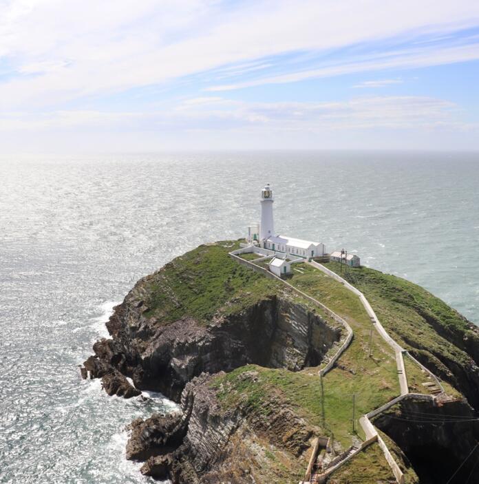 A lighthouse at the end of a green peninsula of land surrounded by a glittering sea